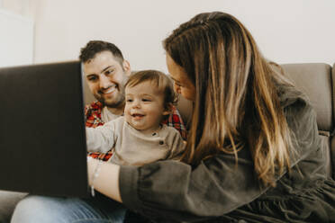 Happy parents with son sitting on sofa during video call at home - GMCF00237