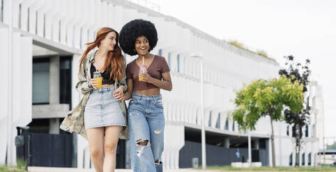 Surprised Afro woman holding hands of female friend while walking in city - JCCMF03385