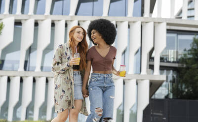 Afro woman laughing while walking with female friend in city - JCCMF03389