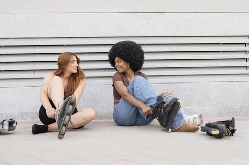 Lächelnde Freundinnen, die sich beim Tragen von Inline-Skates auf dem Fußweg anschauen - JCCMF03392