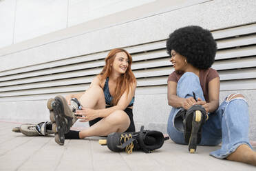 Happy female friends wearing inline skates on footpath - JCCMF03393