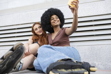 Lächelnde Afro-Frau, die ein Selfie mit einer Freundin vor einer Wand macht - JCCMF03394