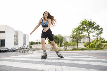 Smiling young redhead woman skating on road in city - JCCMF03397