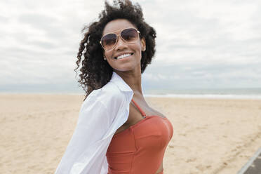 Lächelnde junge Frau, die wegschaut, während sie am Strand steht - JRVF01264