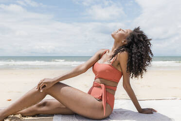 Woman with eyes closed enjoying sunbathing at beach during sunny