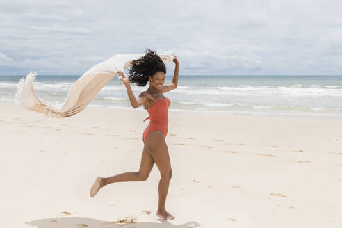 Lächelnde Frau läuft mit Handtuch am Strand - JRVF01286