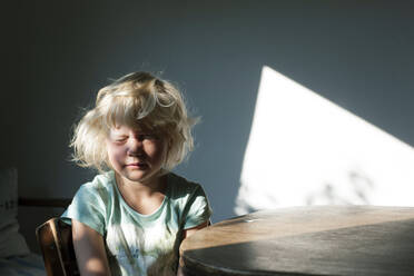 Nettes Mädchen mit Sonnenlicht im Gesicht sitzt am Tisch in der Küche - GISF00830