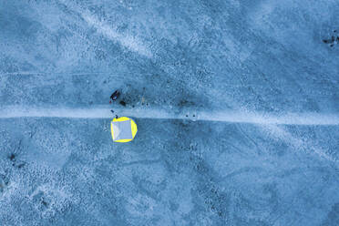 Luftaufnahme einer Person, die in einem gelben technischen Winterzelt über der zugefrorenen Flussmündung im Kauno Mariu Nationalpark in der Nähe von Kaunas, Litauen, übernachtet. - AAEF12811