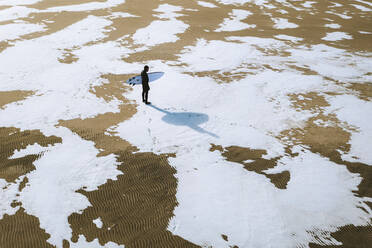 Luftaufnahme eines Surfers am schneebedeckten Strand von Smiltyne in einem sonnigen Wintertag, Klaipeda, Litauen. - AAEF12852