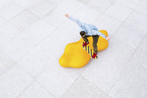 Aerial view of professional skateboarder jumping over the modern yellow object in urban skate park in Kaunas, Lithuania. - AAEF12902