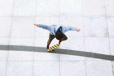 Luftaufnahme eines professionellen Skateboarders, der einen Kickflip-Trick im städtischen Hintergrund auf dem zentralen Platz in Kaunas, Litauen, ausführt. - AAEF12908