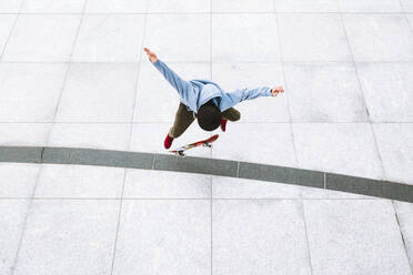 Luftaufnahme eines professionellen Skateboarders, der einen Kickflip-Trick im städtischen Hintergrund auf dem zentralen Platz in Kaunas, Litauen, ausführt. - AAEF12909