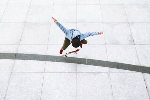 Luftaufnahme eines professionellen Skateboarders, der einen Kickflip-Trick im städtischen Hintergrund auf dem zentralen Platz in Kaunas, Litauen, ausführt. - AAEF12909