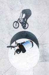 Luftaufnahme der Silhouette eines BMX-Radfahrers, der einen Barspin-Trick auf einer Betonfläche im Skatepark in Panevezys, Litauen, ausführt. - AAEF12947