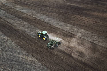 Aerial view of tractor harrowing agricultural dirt field in farming land near Kaunas, Lithuania. - AAEF12986