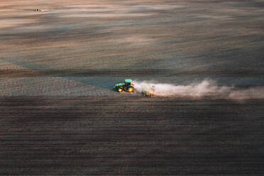 Luftaufnahme eines Traktors bei der Arbeit auf einem landwirtschaftlichen Feld beim Eggen des Bodens im Frühling in der Nähe von Kaunas, Litauen. - AAEF12990