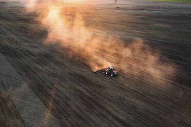 Luftaufnahme von Feldern mit einem Traktor und goldenen Staubwolken hinter ihm in der Nähe von Kaunas, Litauen. - AAEF12992