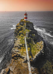 Luftaufnahme von Mayak Na Myse Basargina, einem Leuchtturm auf einer felsigen Landzunge mit Blick auf die Bucht bei Sonnenaufgang in Wladiwostok, Russland. - AAEF13117