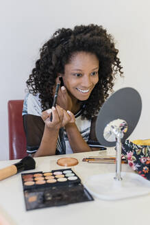 Smiling beauty expert holding make-up brush while looking at mirror - JRVF01315