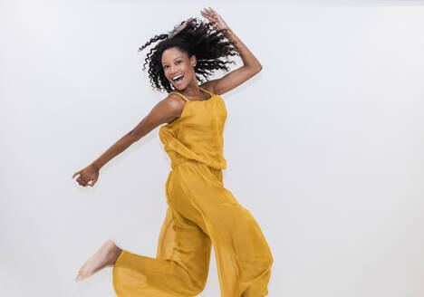 Carefree woman dancing while jumping on white background - JRVF01341