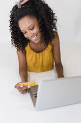 Frau hält Kreditkarte und benutzt Laptop auf weißem Hintergrund - JRVF01345