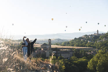 Spanien, Kastilien und Leon, Segovia, Zwei Schwestern machen ein Selfie mit fliegenden Heißluftballons und historischen Gebäuden der Stadt - JAQF00693