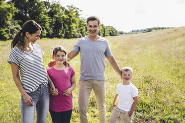 Lächelnde Eltern stehen mit Kindern auf einer Wiese an einem sonnigen Tag - UUF24194