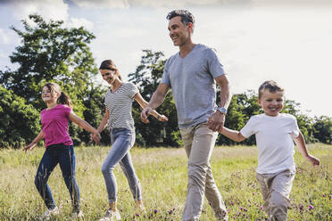 Smiling family holding hands while walking on grass - UUF24195