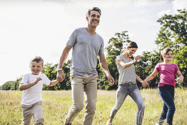 Familie hält sich beim Laufen auf der Wiese an den Händen - UUF24196