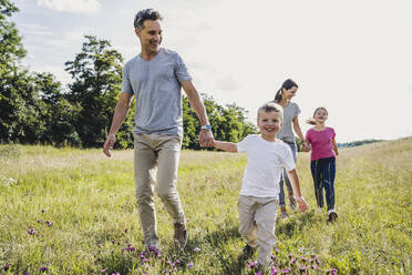 Parents holding hands of children while walking on grass - UUF24197