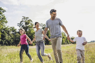 Playful family holding hands while running on grass - UUF24198