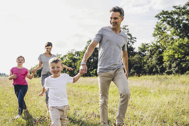 Children holding hands of parents while walking at meadow - UUF24200