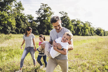 Lächelnder Vater trägt seinen Sohn beim Spaziergang mit der Familie auf einer Wiese - UUF24201