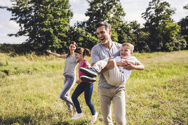 Man carrying boy while walking with woman and girl on grass - UUF24202