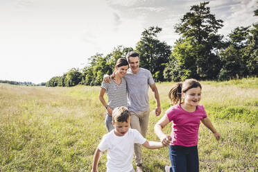 Eltern, die hinter ihren Kindern laufen, während sie sich im Gras an den Händen halten - UUF24204