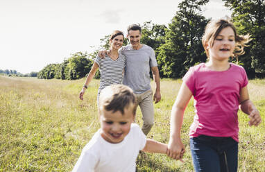 Smiling parents looking at playful children running on meadow - UUF24205