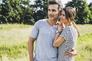 Man with arm around on smiling woman standing at meadow - UUF24211