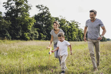 Parents running behind son holding toy airplane on grass - UUF24218