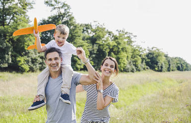 Smiling man carrying boy on shoulders by woman at meadow - UUF24220