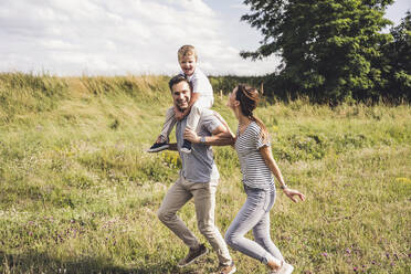 Frau läuft mit Familie im Gras an einem sonnigen Tag - UUF24223