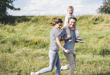 Smiling family running together at meadow - UUF24224