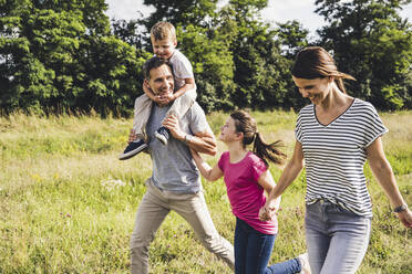 Happy family holding hands while running on grass - UUF24227