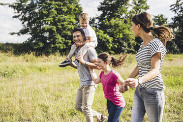 Happy family holding hands while running on grass during sunny day - UUF24228