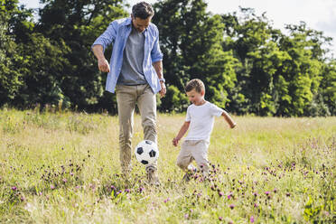 Mann, der mit einem Jungen auf einer Wiese in der Sonne Fußball spielt - UUF24230