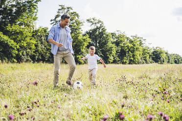 Father and son playing with soccer ball on meadow - UUF24231