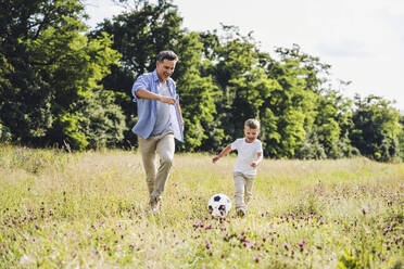 Cheerful father and son playing soccer on grass - UUF24232