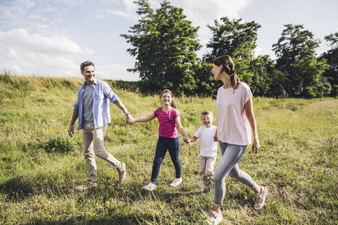 Lächelnde Familie, die sich beim Spazierengehen im Gras an den Händen hält - UUF24233