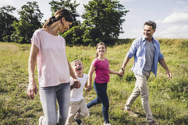 Children holding hands of parents while walking at meadow - UUF24234