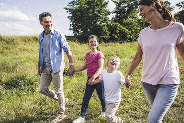 Fröhliche Kinder schauen ihre Mutter an, während sie im Gras laufen - UUF24235