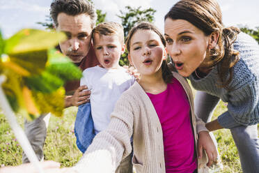 Familie bläst gemeinsam Windradspielzeug an einem sonnigen Tag - UUF24238